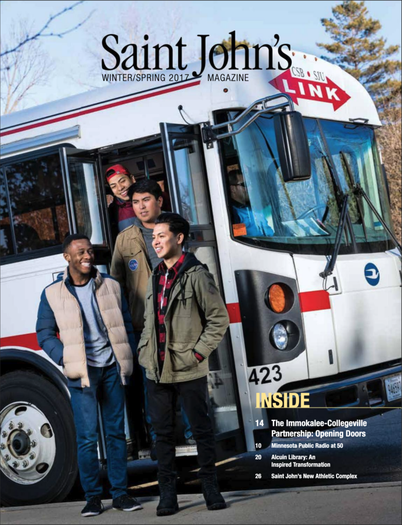 Four people stand outside a St. John's University bus, smiling. They wear winter clothing, indicating cold weather. The bus is labeled "Link" and features the university's logo. The magazine cover includes feature titles related to Saint John's activities.